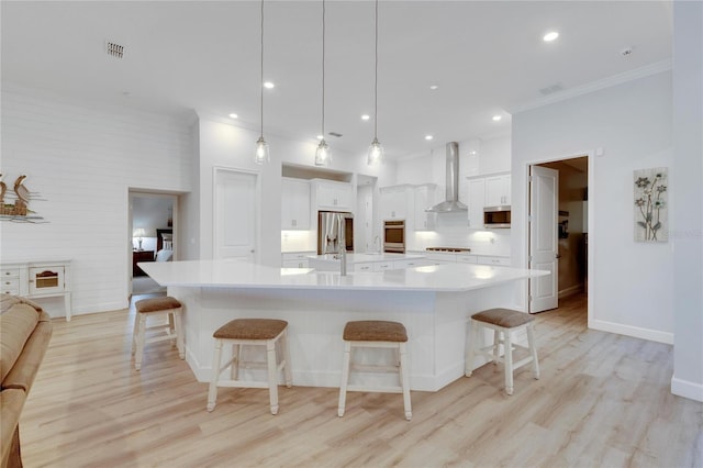 kitchen with a breakfast bar, white cabinets, hanging light fixtures, a large island with sink, and wall chimney exhaust hood