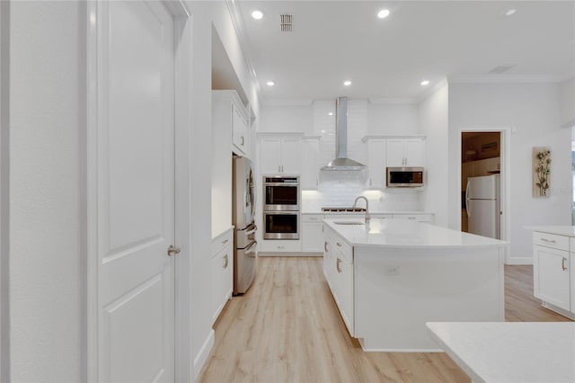 kitchen with tasteful backsplash, white cabinetry, appliances with stainless steel finishes, an island with sink, and wall chimney range hood