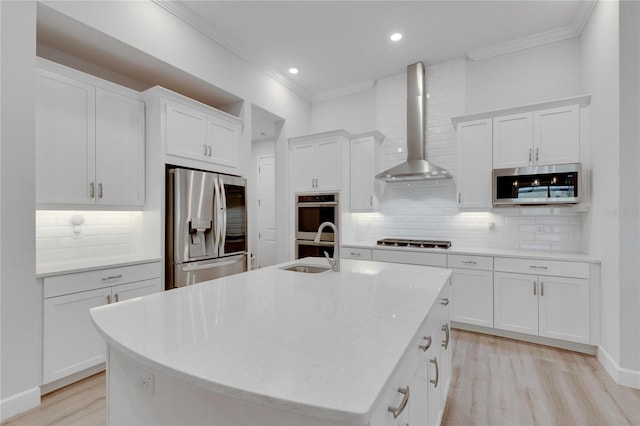 kitchen with wall chimney range hood, sink, stainless steel appliances, an island with sink, and white cabinets