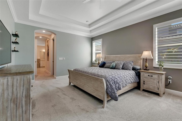 carpeted bedroom with a raised ceiling, ceiling fan, crown molding, and ensuite bath