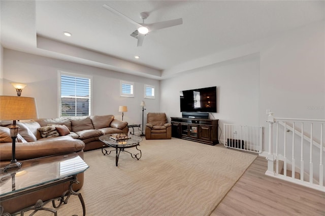 living room with ceiling fan, light wood-type flooring, and a tray ceiling