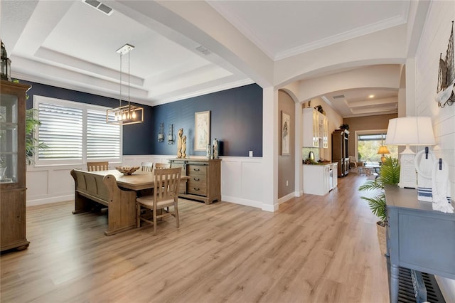 dining room featuring crown molding, light hardwood / wood-style floors, a raised ceiling, and a chandelier