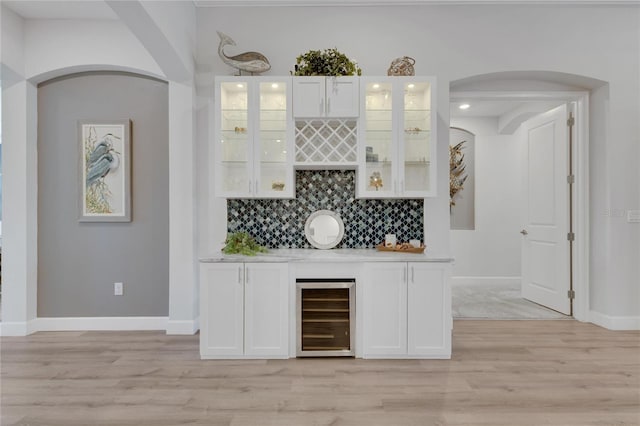 bar with wine cooler, white cabinetry, tasteful backsplash, and light hardwood / wood-style flooring