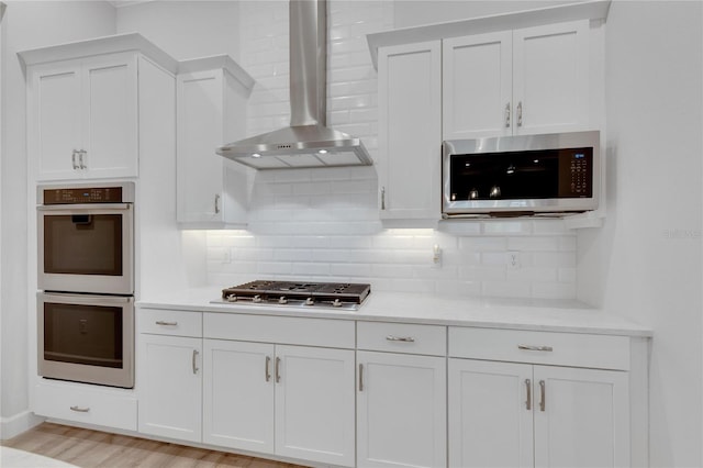 kitchen featuring white cabinetry, stainless steel appliances, and wall chimney exhaust hood