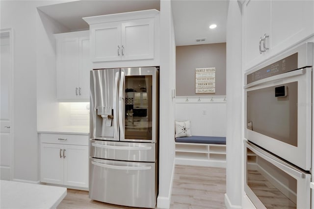 kitchen featuring white cabinetry, stainless steel fridge with ice dispenser, double oven, and light wood-type flooring