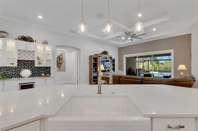 kitchen featuring backsplash, hanging light fixtures, coffered ceiling, ceiling fan, and light stone countertops