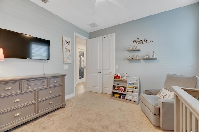 bedroom featuring a crib, light colored carpet, a closet, and ceiling fan