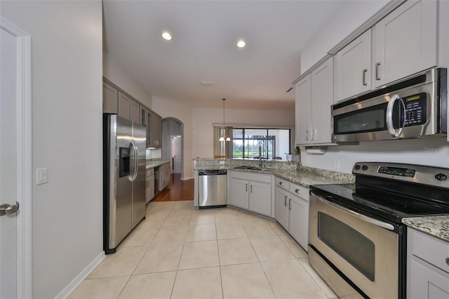 kitchen with hanging light fixtures, stainless steel appliances, kitchen peninsula, light tile patterned flooring, and light stone counters