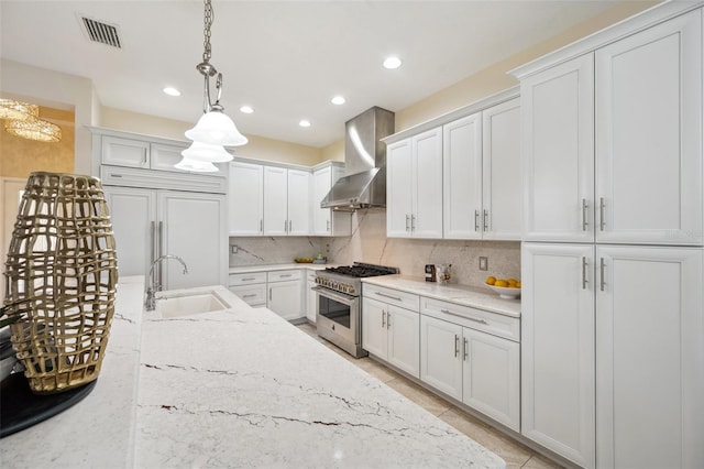 kitchen with sink, pendant lighting, wall chimney range hood, premium appliances, and white cabinets