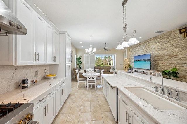 kitchen with tasteful backsplash, hanging light fixtures, light stone counters, white cabinets, and sink