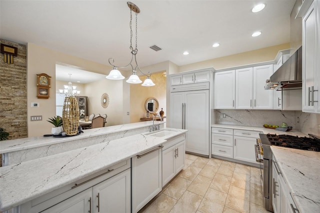 kitchen with sink, white cabinets, high quality appliances, wall chimney range hood, and pendant lighting