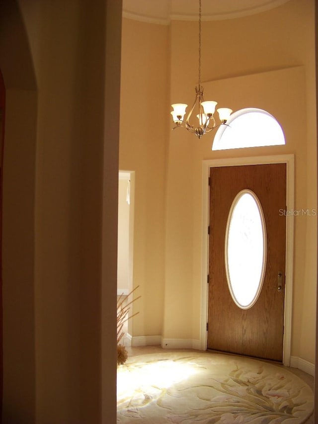 entryway with ornamental molding, carpet, and a notable chandelier