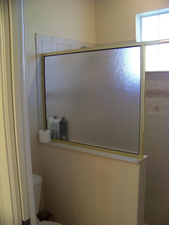 bathroom featuring a shower with shower door and toilet