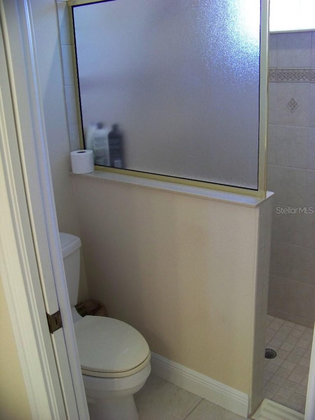 bathroom featuring tiled shower, toilet, and tile patterned flooring