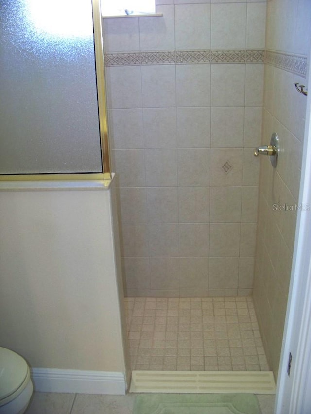 bathroom with a tile shower, toilet, and tile patterned flooring