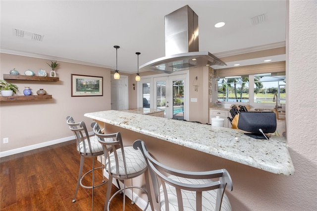 kitchen featuring a breakfast bar area, island range hood, dark wood-type flooring, french doors, and decorative light fixtures