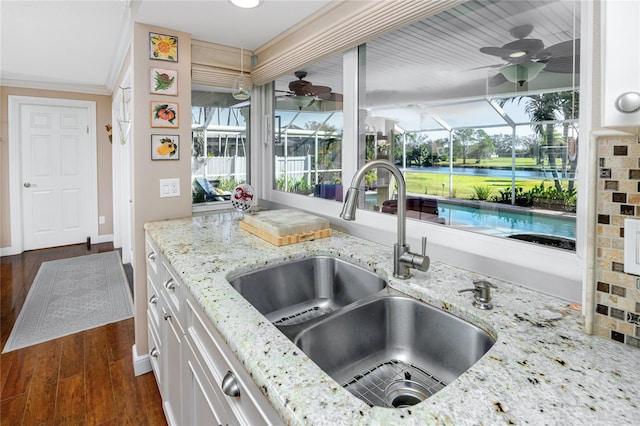 kitchen with light stone countertops, sink, white cabinets, ornamental molding, and dark hardwood / wood-style floors