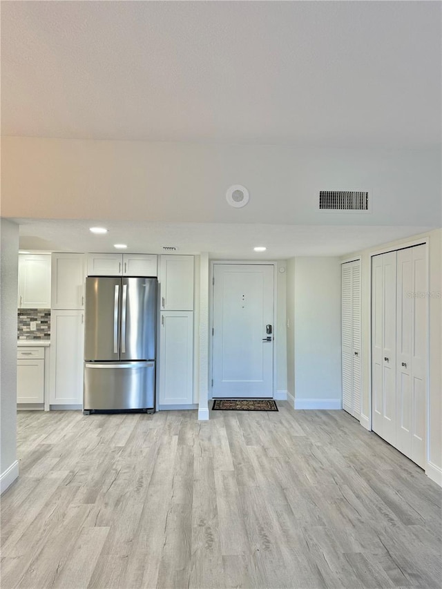 kitchen featuring white cabinets, light hardwood / wood-style floors, backsplash, and stainless steel fridge