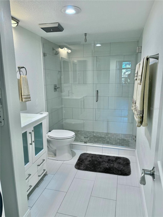 bathroom with vanity, toilet, a textured ceiling, and a shower with shower door