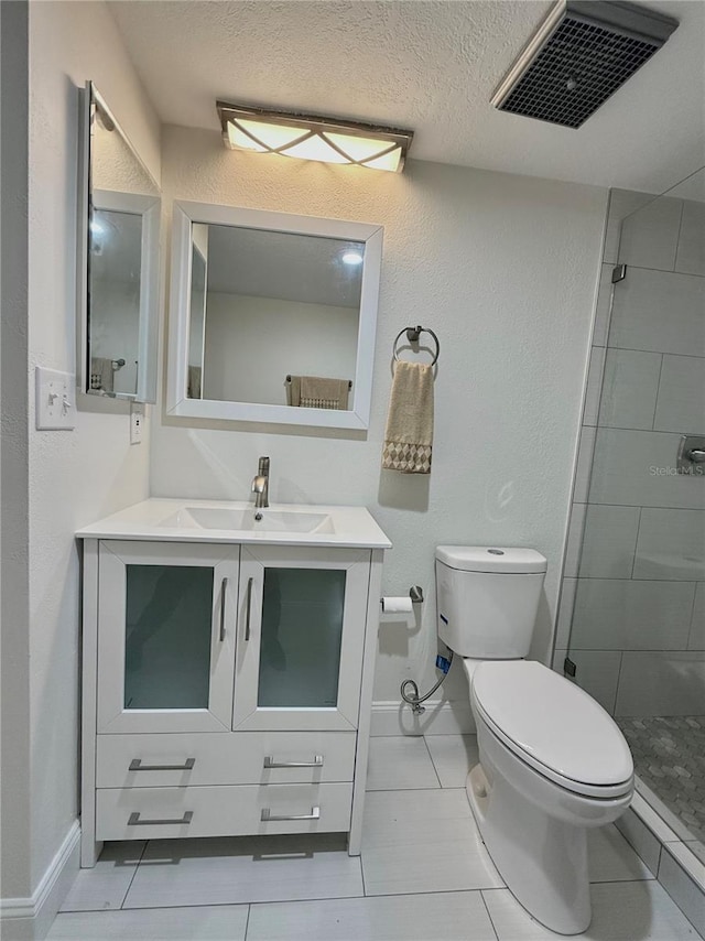 bathroom featuring toilet, tile patterned flooring, vanity, a tile shower, and a textured ceiling