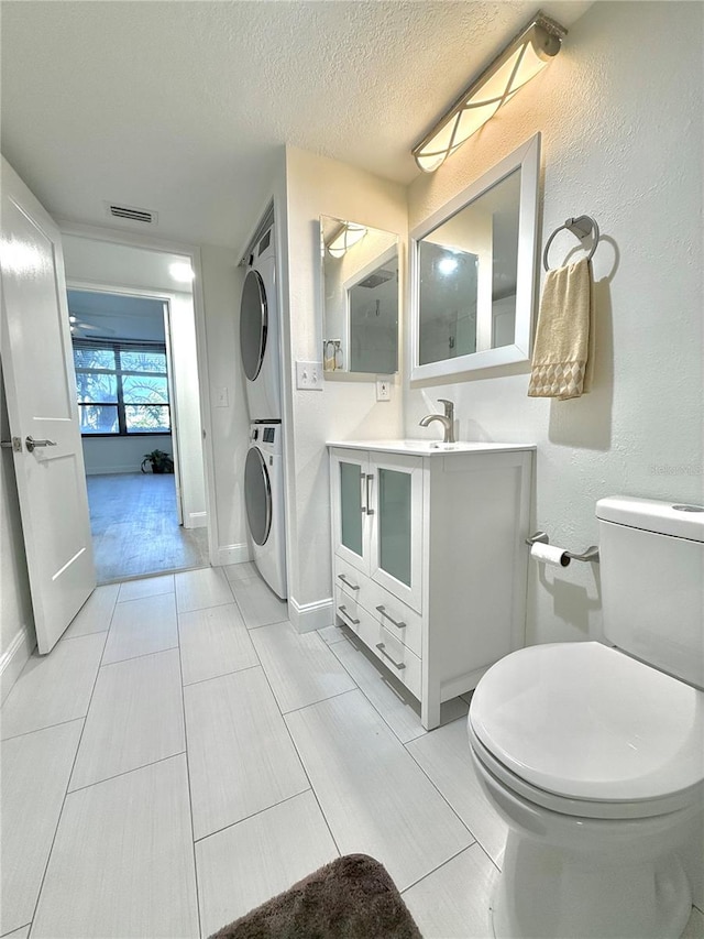 bathroom with a textured ceiling, toilet, stacked washer and dryer, vanity, and tile patterned flooring