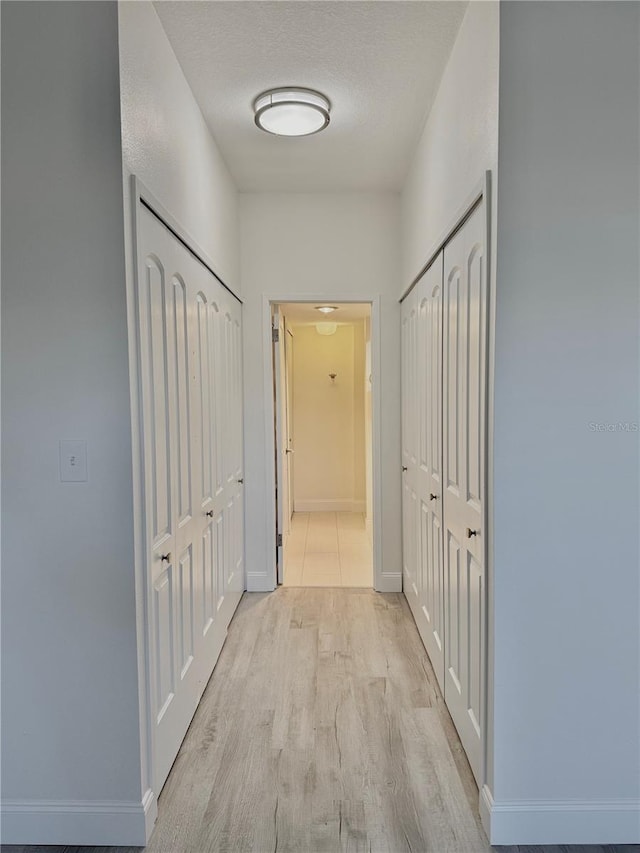 hall with a textured ceiling and light hardwood / wood-style flooring