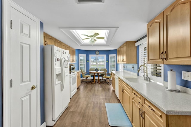 kitchen featuring white appliances, a skylight, sink, light hardwood / wood-style floors, and wooden walls