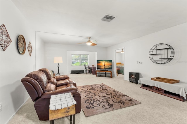 carpeted living room featuring ceiling fan and a wood stove