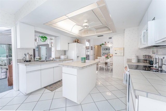 kitchen with white appliances, a kitchen island, tile countertops, ceiling fan, and white cabinets