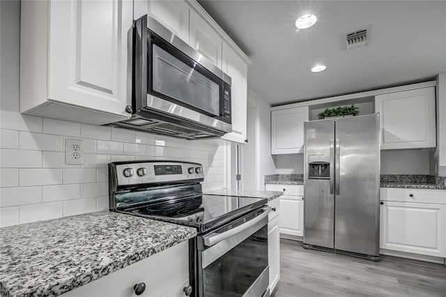 kitchen featuring backsplash, light stone countertops, white cabinetry, light wood-type flooring, and appliances with stainless steel finishes