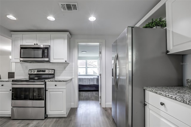 kitchen with white cabinets, light stone countertops, light hardwood / wood-style flooring, and appliances with stainless steel finishes