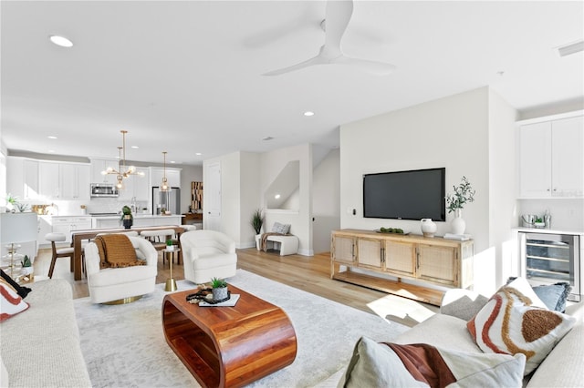 living room with beverage cooler, ceiling fan with notable chandelier, and light wood-type flooring