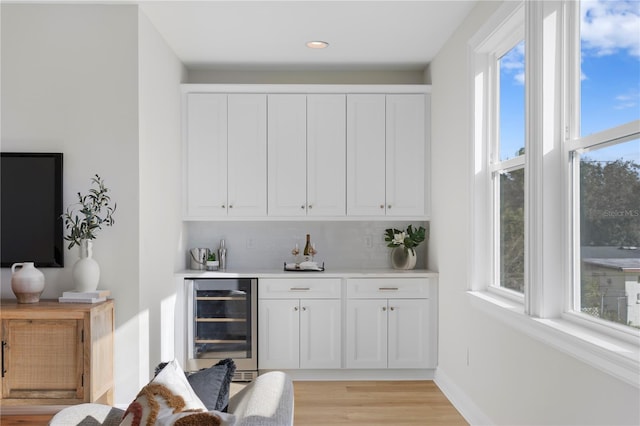 bar featuring light wood-type flooring, backsplash, white cabinetry, and wine cooler