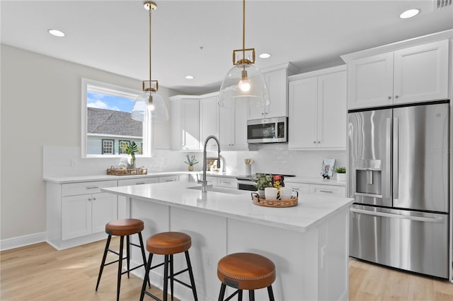 kitchen with pendant lighting, a kitchen island with sink, white cabinets, light hardwood / wood-style floors, and stainless steel appliances