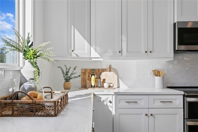 kitchen with tasteful backsplash, white cabinets, and appliances with stainless steel finishes