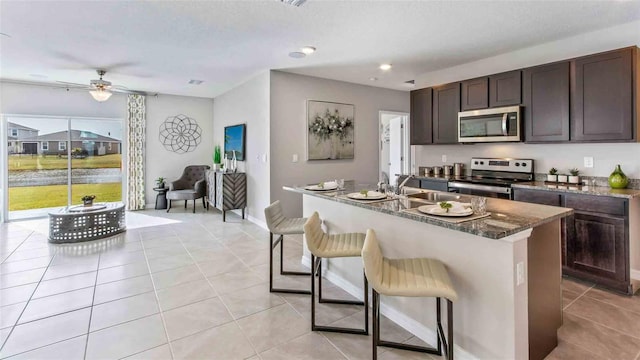 kitchen with ceiling fan, sink, stainless steel appliances, a kitchen island with sink, and a breakfast bar