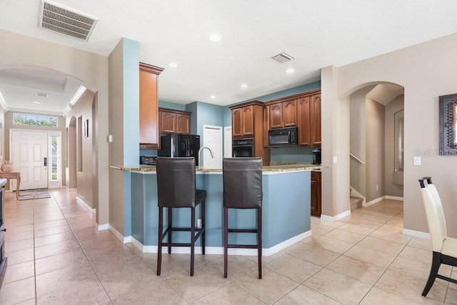 kitchen with crown molding, black appliances, light stone counters, and a breakfast bar area