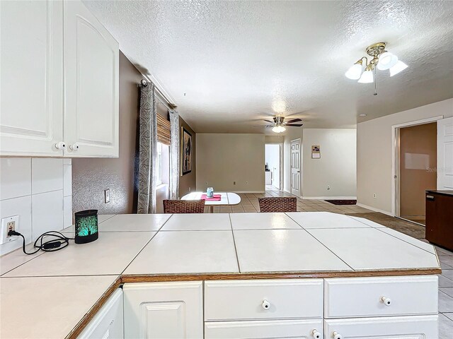 kitchen with white cabinets, light tile patterned floors, ceiling fan, a textured ceiling, and tile counters