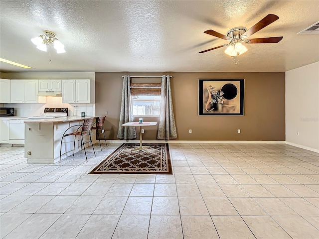 kitchen featuring white cabinets, ceiling fan, a textured ceiling, a kitchen bar, and white stove