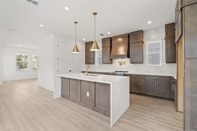 kitchen with sink, light wood-type flooring, an island with sink, electric range, and premium range hood