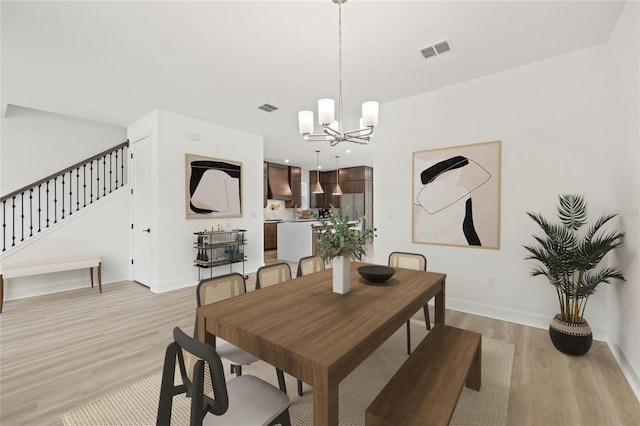dining space featuring light wood-style floors, a notable chandelier, stairs, and visible vents