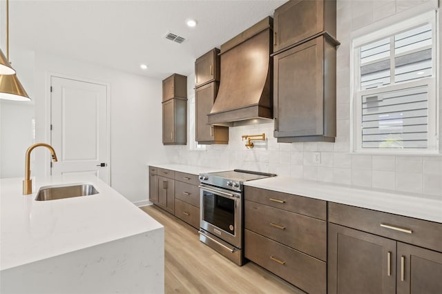 kitchen with stainless steel range with electric stovetop, light countertops, custom range hood, a sink, and light wood finished floors