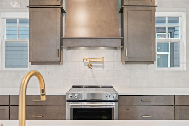 kitchen featuring light countertops, decorative backsplash, custom range hood, and stainless steel electric range
