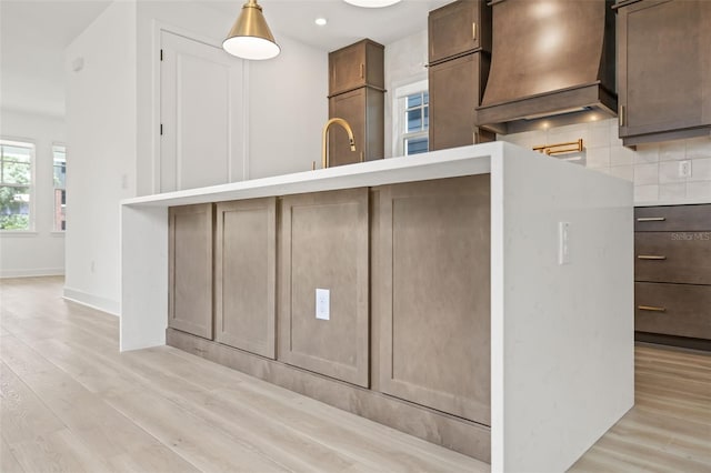 kitchen featuring pendant lighting, light hardwood / wood-style floors, custom exhaust hood, and backsplash