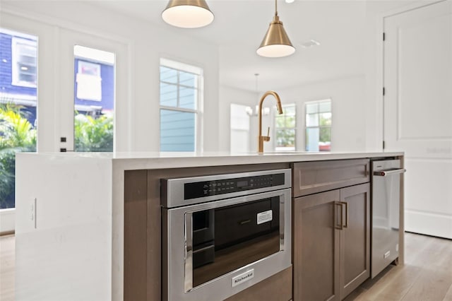 kitchen featuring a healthy amount of sunlight, light countertops, hanging light fixtures, and light wood finished floors