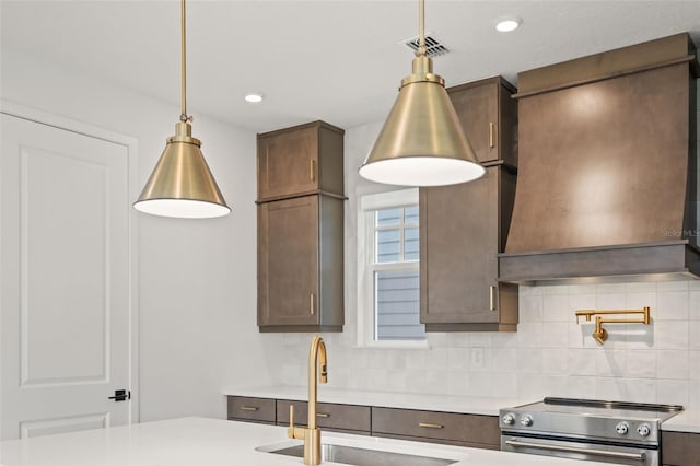 kitchen featuring sink, stainless steel range, custom range hood, and decorative light fixtures