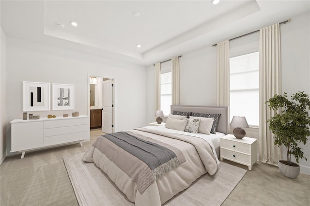 carpeted bedroom with ensuite bath and a tray ceiling