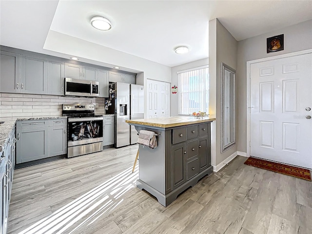 kitchen with decorative backsplash, appliances with stainless steel finishes, gray cabinetry, and light wood-type flooring