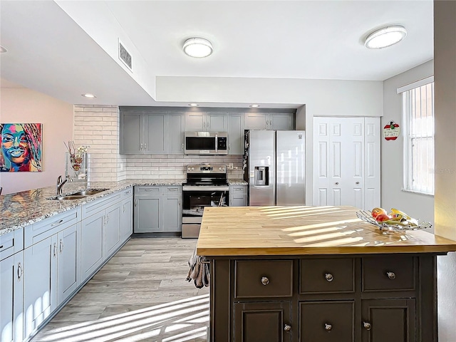 kitchen with tasteful backsplash, appliances with stainless steel finishes, sink, wood counters, and light hardwood / wood-style flooring