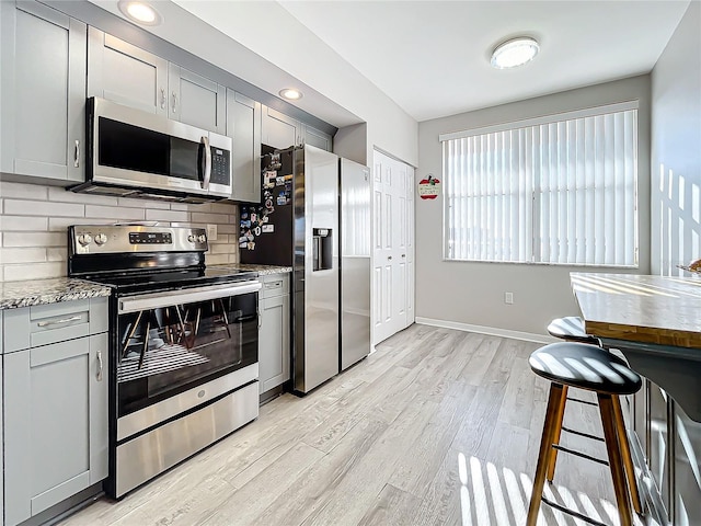 kitchen with light stone counters, appliances with stainless steel finishes, light wood-type flooring, and gray cabinets